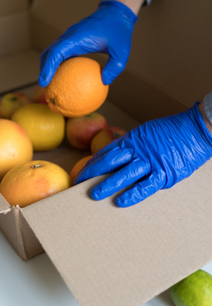 Volunteer,In,Protective,Medical,Gloves,Putting,Fruits,In,Donation,Box.